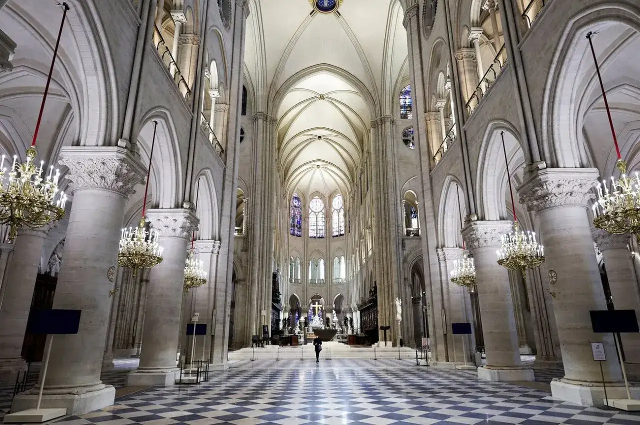 Wnętrze katedry Notre Dame, z monumentalnymi filarami, sklepieniami i witrażami. Na pierwszym planie szachownicowa posadzka.
