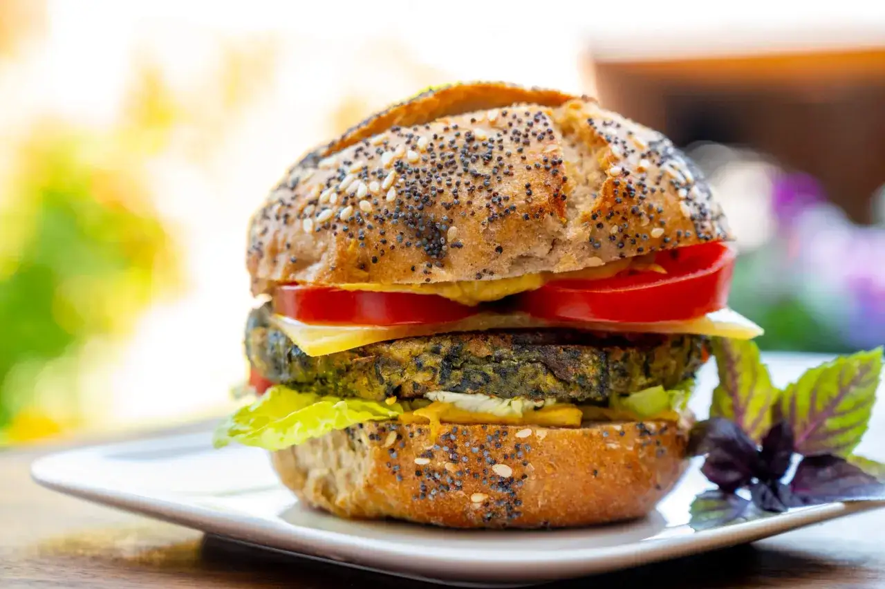 Deliciosa hamburguesa de espinacas con pan de semillas, queso, tomate y lechuga, servida en un plato blanco.