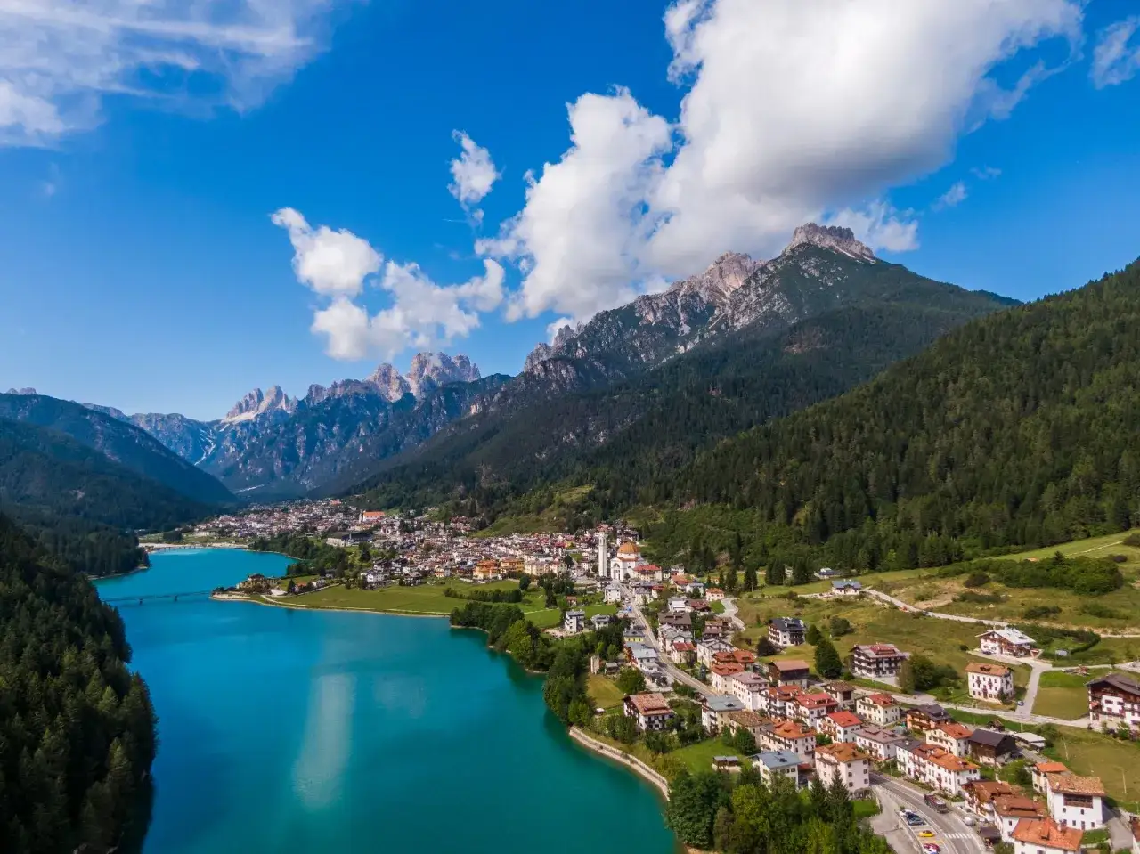 Vista aerea del **lago Auronzo di Cadore** con le montagne sullo sfondo e il paese che si affaccia sull'acqua turchese.