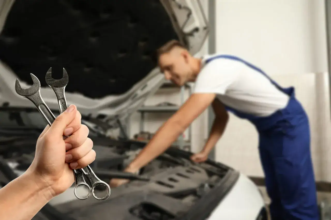 Mano sostiene llaves inglesas. Mecánico revisa motor de coche que no arranca.