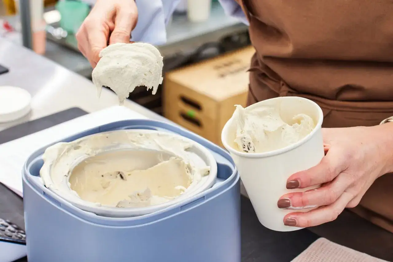 Milcheis selber machen mit Eismaschine: Cremiges Eis wird aus dem Behälter geschöpft und in einen Becher gefüllt.