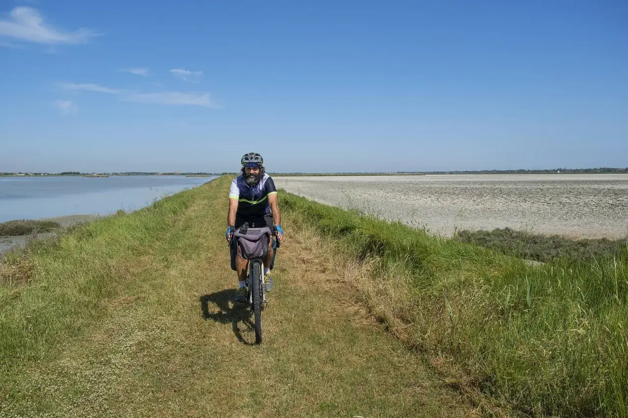 Uomo in bici su sterrato, con acqua a sinistra e saline a destra, un classico percorso in bici a Cervia.