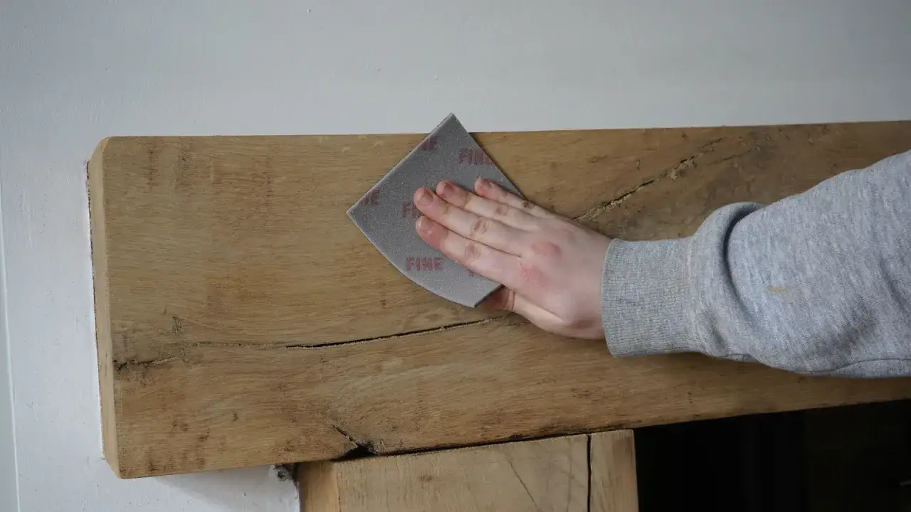 Mano lijando madera r&uacute;stica con lija fina.