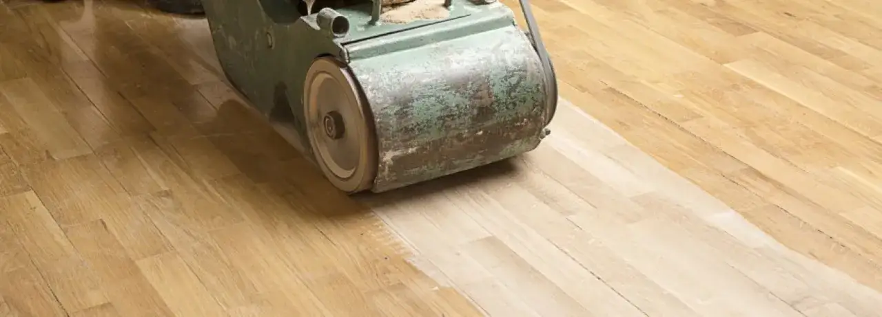 Macchina levigatrice in azione per levigare il parquet, rivelando il legno chiaro sottostante.