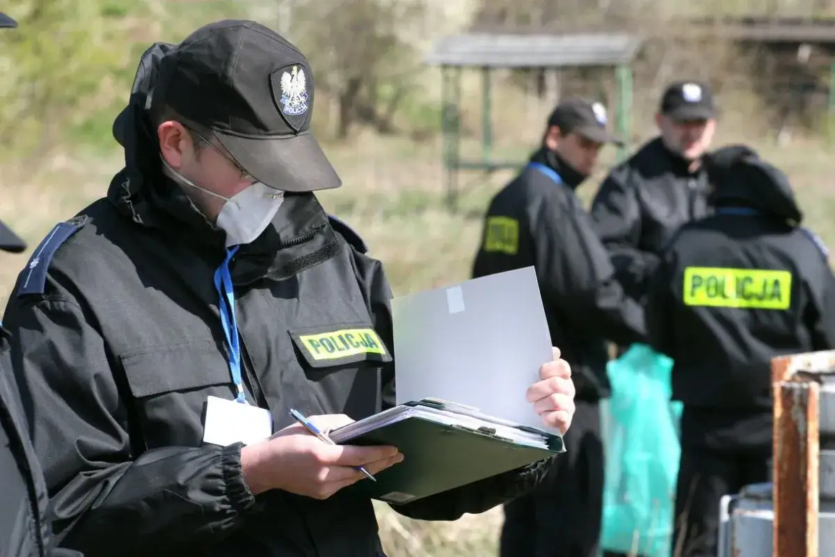 Policjant w masce i czapce z orłem notuje na miejscu zdarzenia. To pierwszy krok, by dowiedzieć się, jak zostać detektywem w policji.