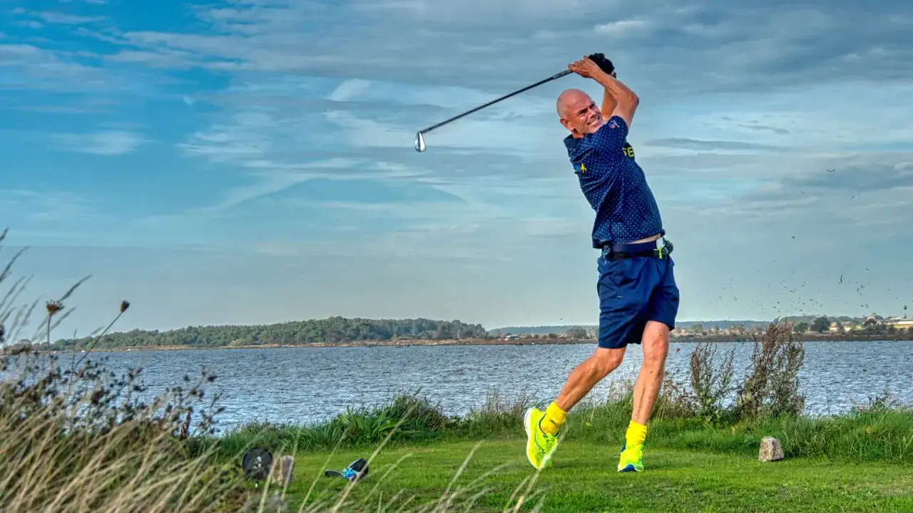 Man i full sving p&aring; golfbanan, redo f&ouml;r en perfekt drive. Vacker utsikt &ouml;ver vattnet.