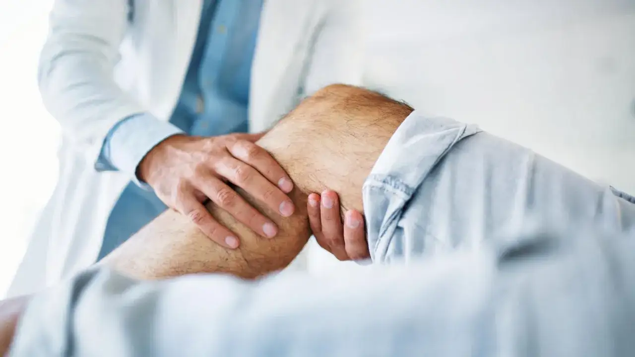 Arzt untersucht Knie eines Mannes. Mögliche Ursache: Wachstumsschmerzen Erwachsene.