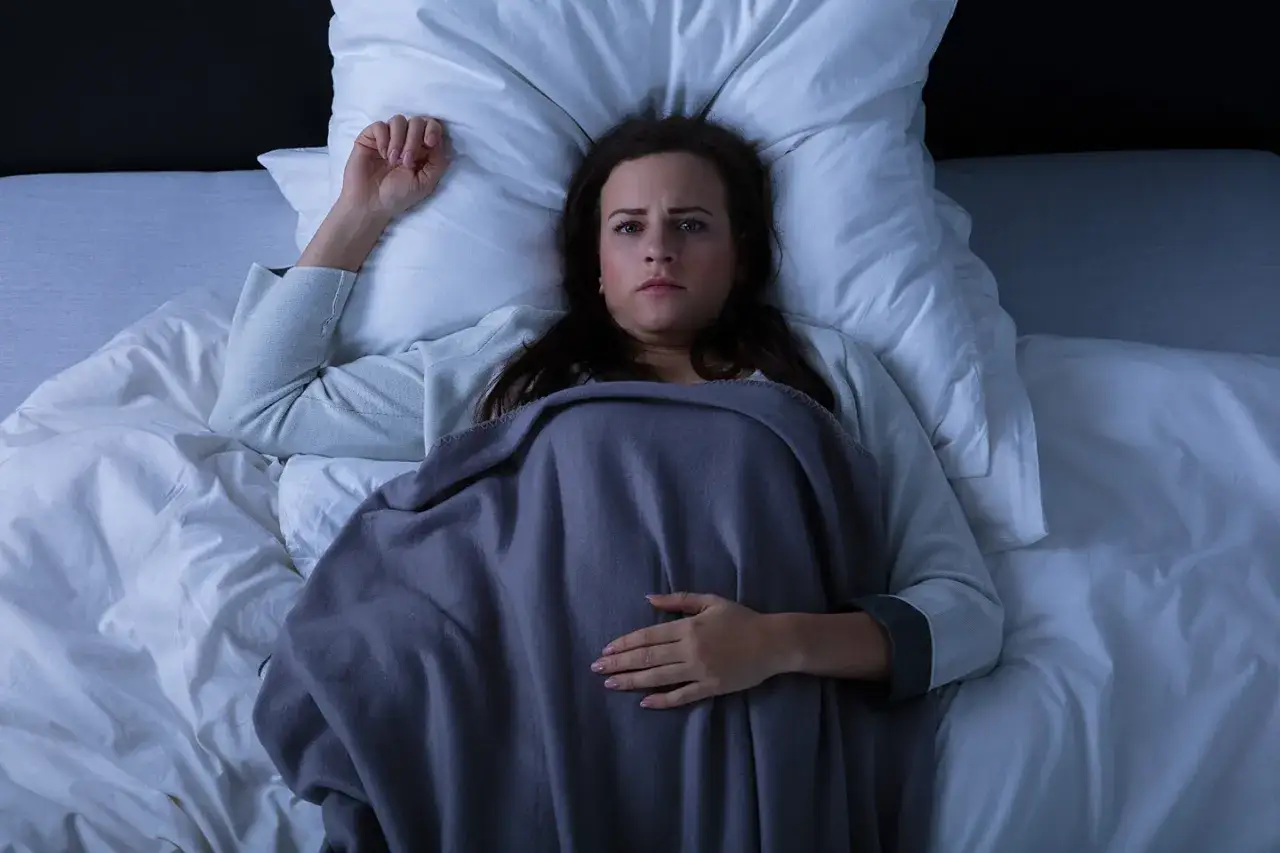 Frau liegt im Bett, &auml;ngstlicher Blick. Sie fragt sich, ob man bei einer Schlafparalyse sterben kann.