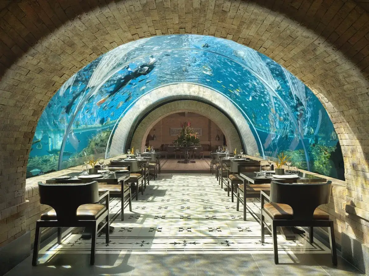 Un restaurant sous la mer, avec des tables dressées et un plongeur nageant parmi les poissons dans un tunnel aquatique spectaculaire.