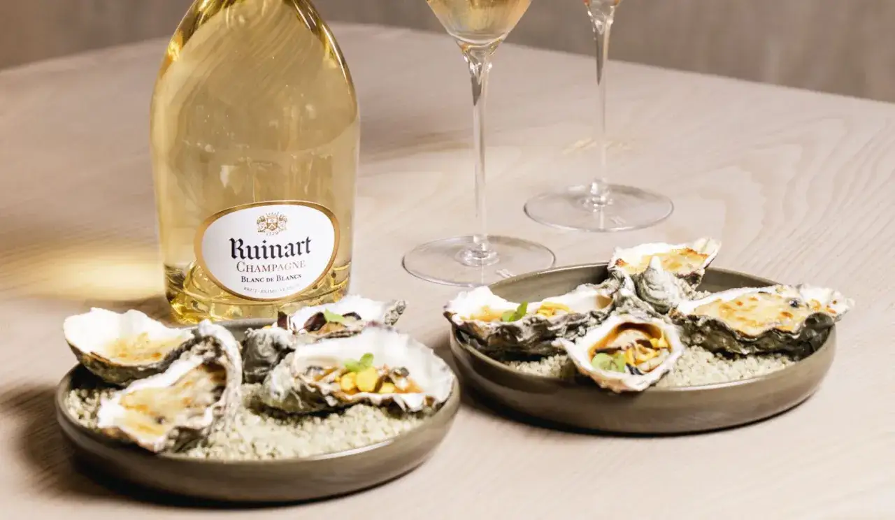 Bouteille de Ruinart Blanc de Blancs, symbole d'&eacute;l&eacute;gance, avec des hu&icirc;tres gratin&eacute;es. Le blanc de blanc signification est ici une exp&eacute;rience gustative raffin&eacute;e.