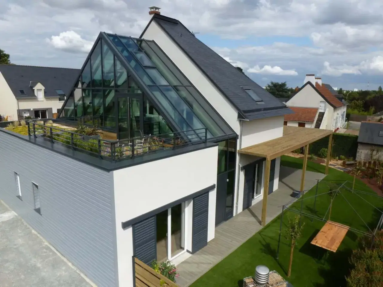 Une maison moderne avec une toiture vitrée spectaculaire, des terrasses végétalisées et un auvent en bois. Ces maisons bioclimatiques allient esthétique et performance énergétique.