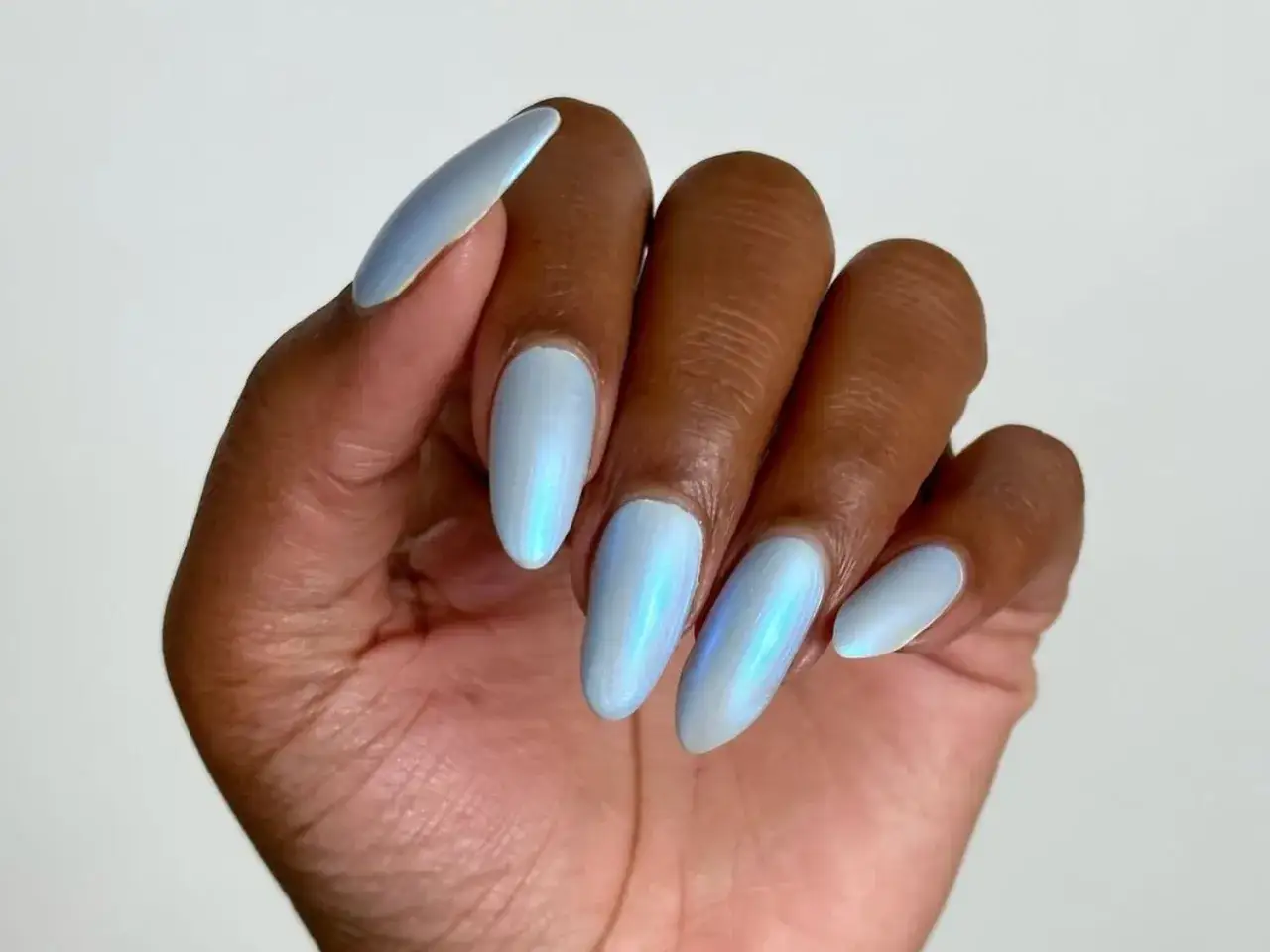 Dłoń z paznokciami w odcieniu baby blue. Kolor paznokci jest opalizujący, z subtelnymi refleksami.