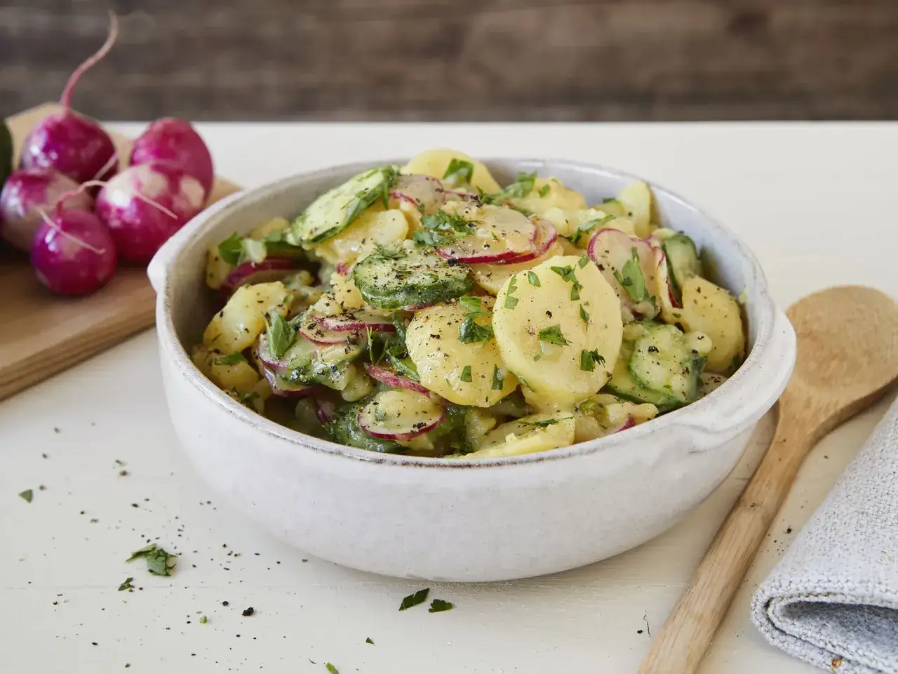 Kartoffelsalat mal anders: Scheiben von Kartoffeln, Gurken und Radieschen mit Kräutern und Pfeffer in einer Schüssel.
