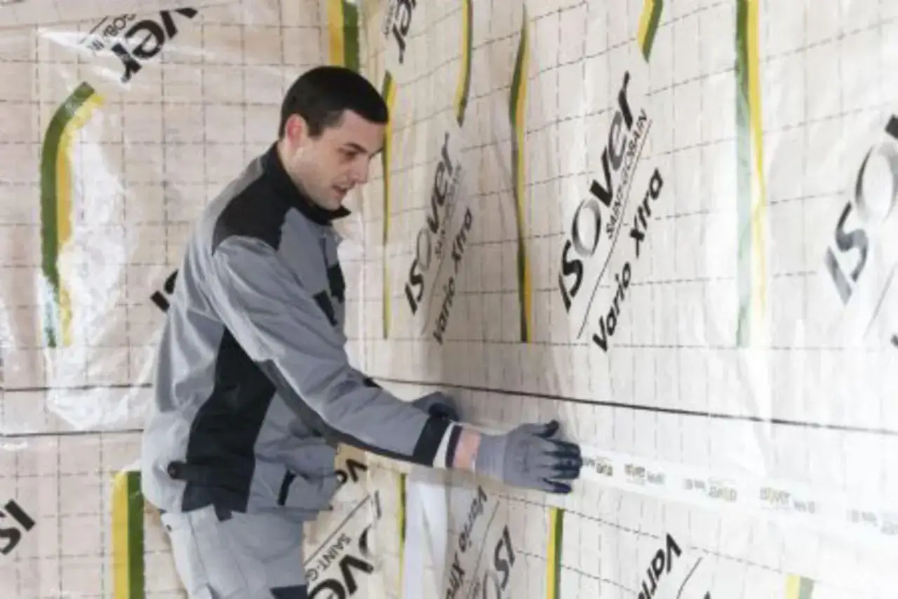 Un ouvrier pose une membrane d'étanchéité pour comment isoler un mur intérieur. La membrane est marquée 