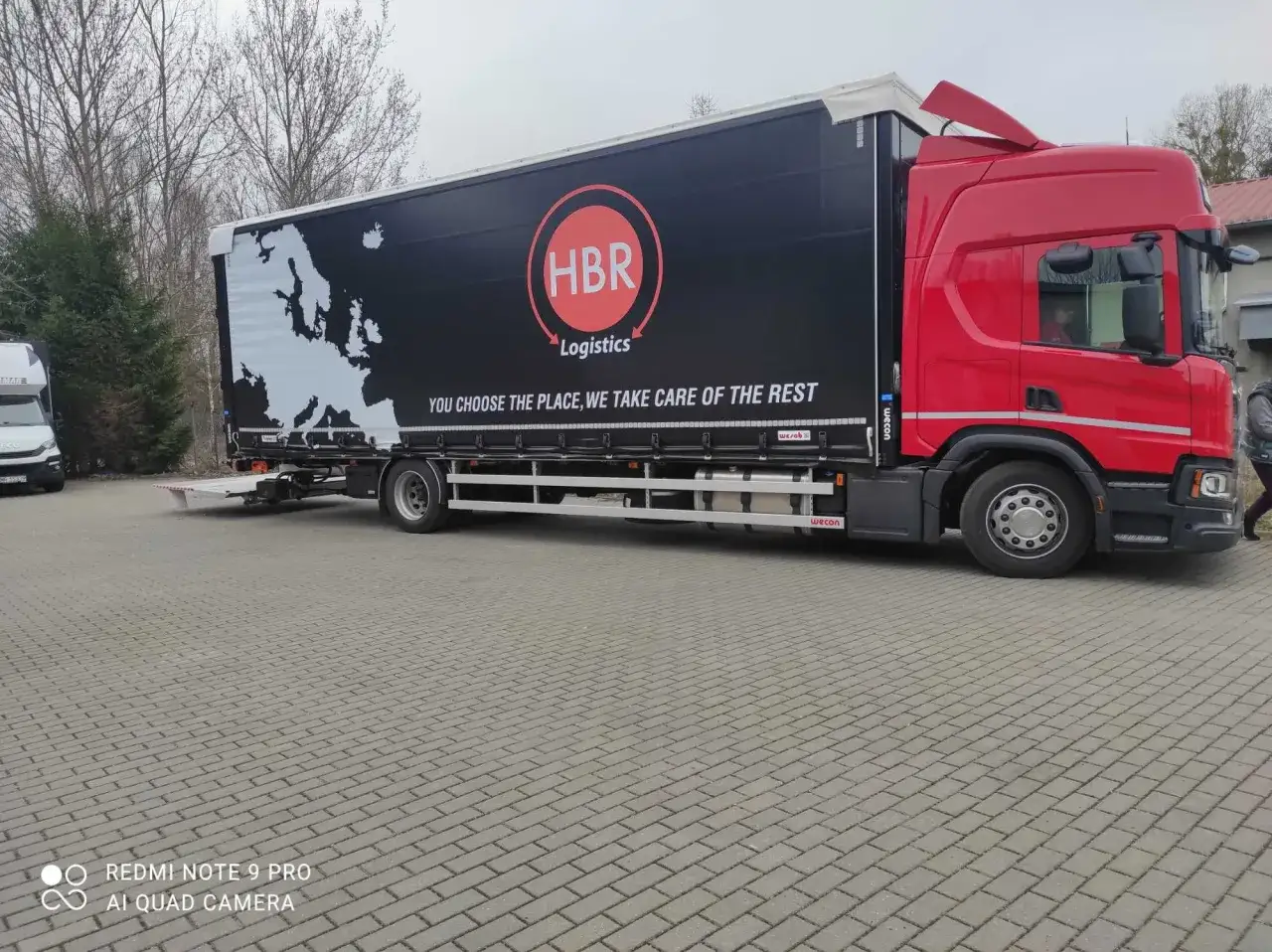 Czerwona ciężarówka HBR Logistics z mapą Europy na naczepie. Oferuje tani transport, dbając o każdy szczegół.