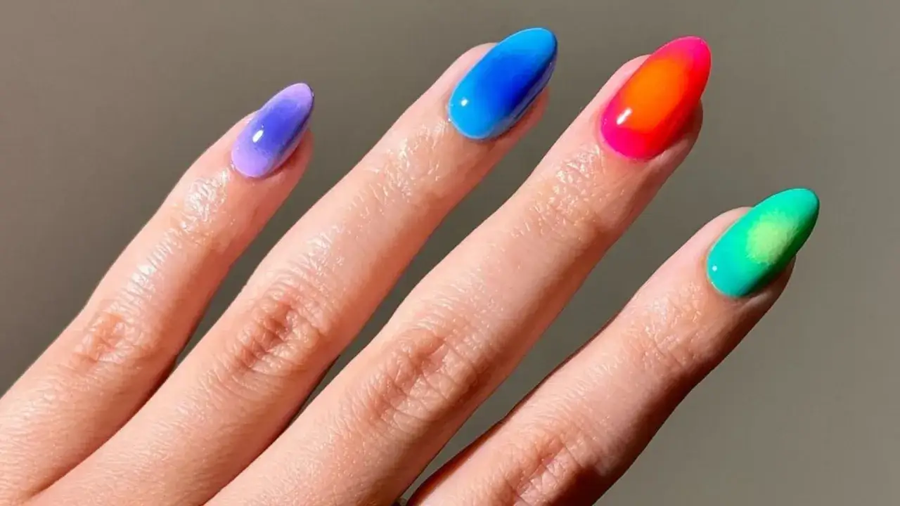 Manicura con **aura nails** degradadas en tonos morado, azul, naranja neón y verde.