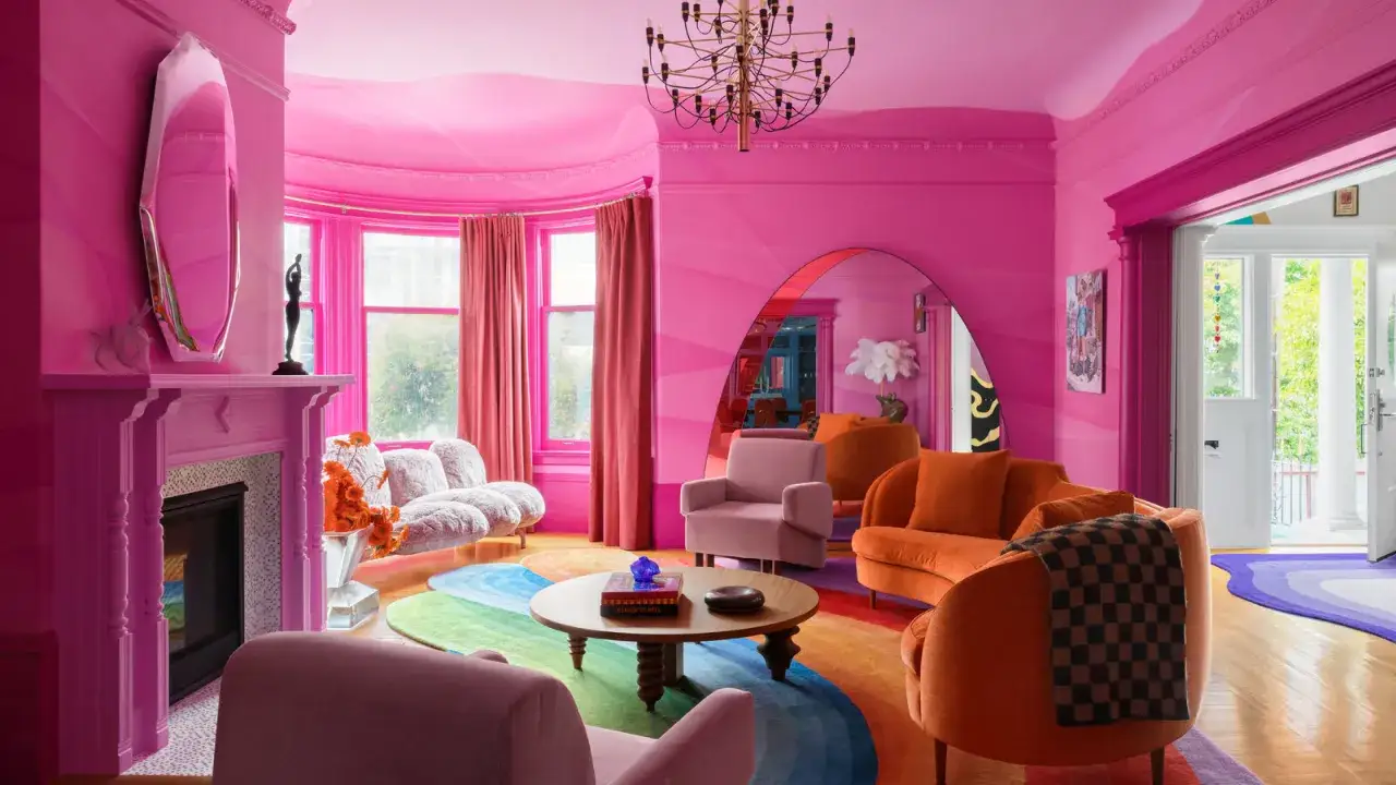 W tym salonie w stylu Barbie, gdzie króluje róż, pomarańczowe meble i tęczowy dywan tworzą odważne połączenie. Jaki kolor pasuje do różowego? Pomarańczowy, jak widać!