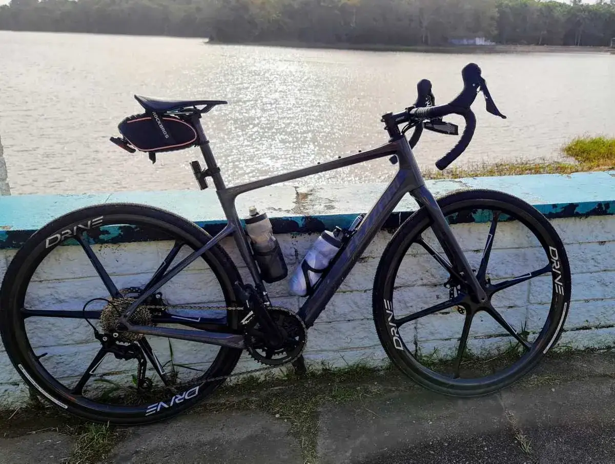 Szary rower szosowy z karbonowymi kołami DRIVE i sakiewką pod siodełkiem, gotowy na wyprawę nad jezioro.