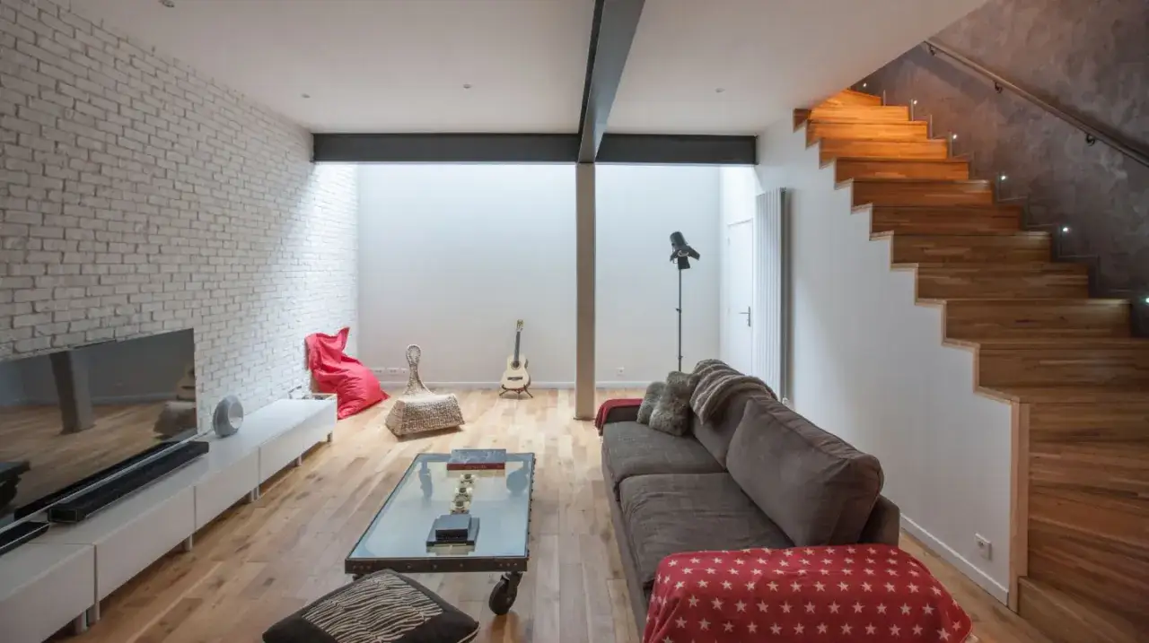 Aménager un sous-sol en pièce habitable : salon moderne avec mur de briques, escalier en bois et mobilier confortable.
