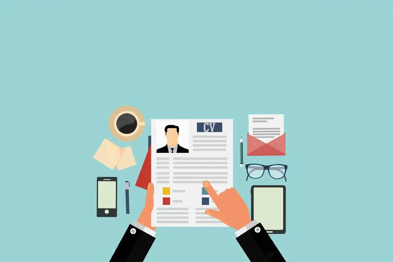 Ręce trzymają CV, przygotowując się do interview. Na stole kawa, telefon i okulary.