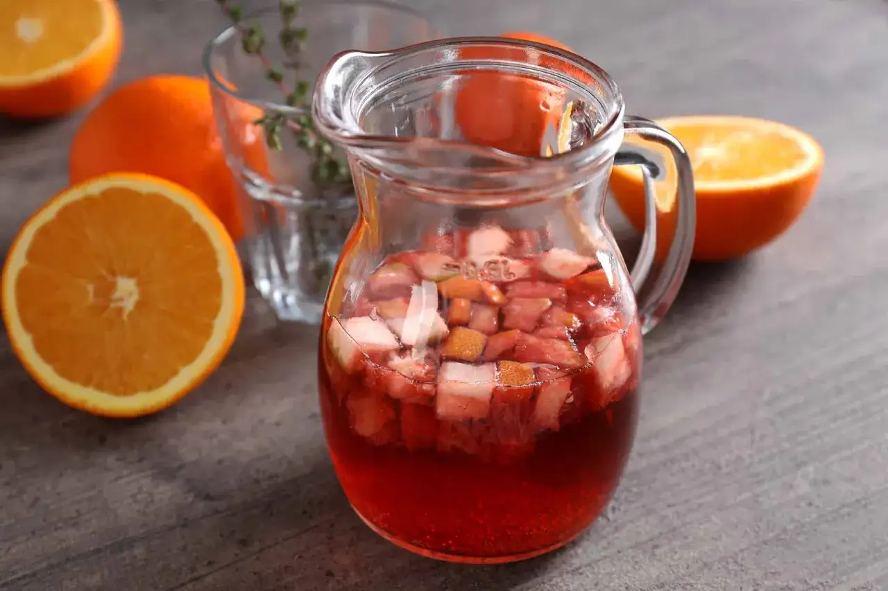 Caraffa di vino per sangria con pezzi di frutta e arance fresche intorno.