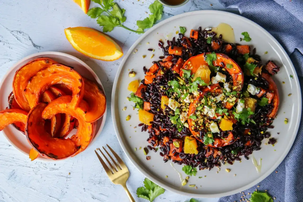 Un plat color&eacute; de riz v&eacute;n&eacute;r&eacute; avec des morceaux de courge r&ocirc;tie, des &eacute;clats d'orange et du fromage &eacute;miett&eacute;, garni de pistaches et de coriandre.