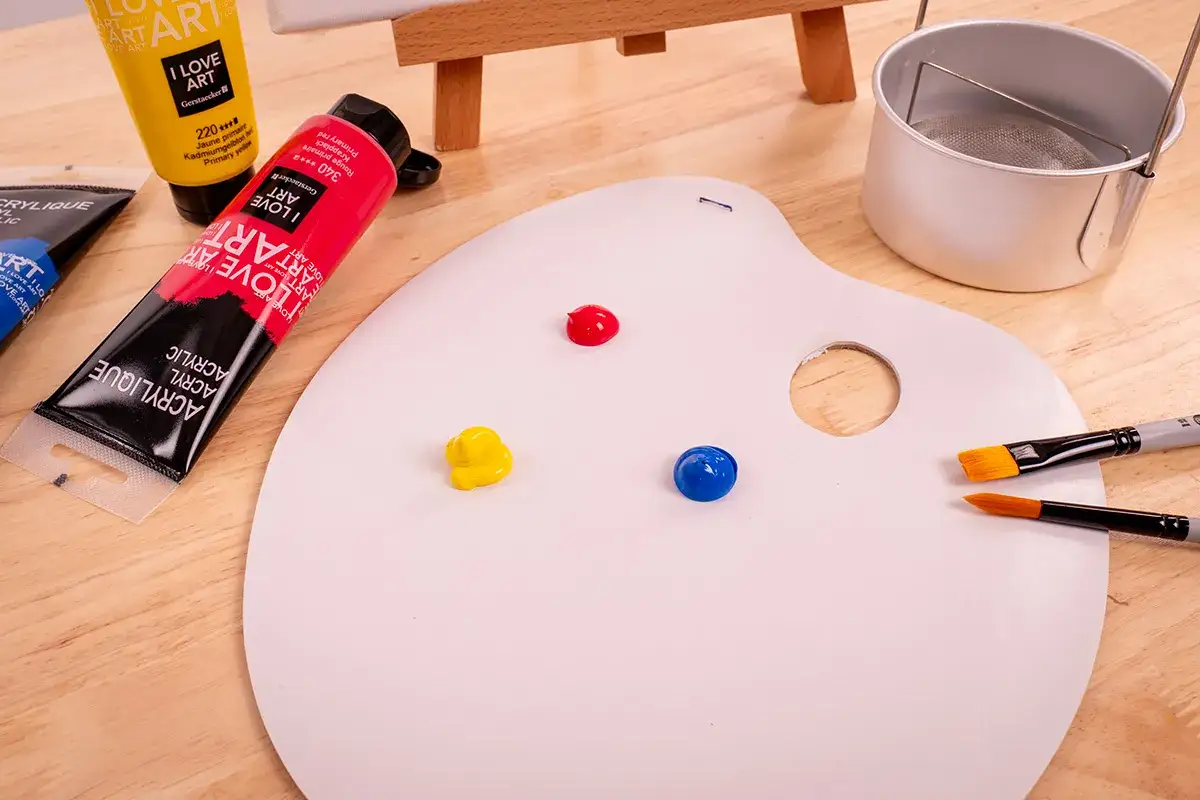 Prêt à se mettre à la peinture : palette blanche avec des touches de peinture rouge, jaune et bleue, des tubes de peinture acrylique et des pinceaux.