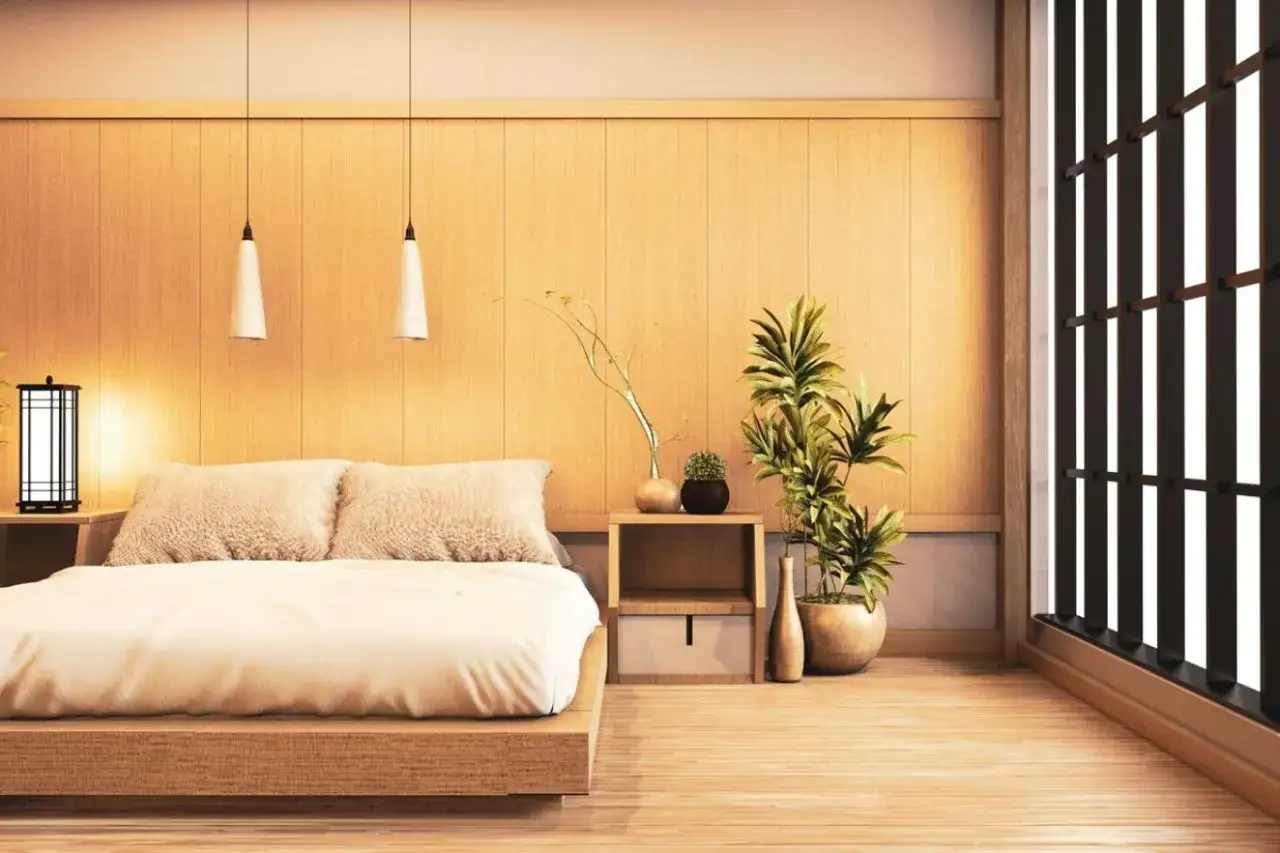 Une chambre style japonais épurée avec un lit bas en bois, des coussins douillets, des plantes vertes et une fenêtre aux persiennes sombres.