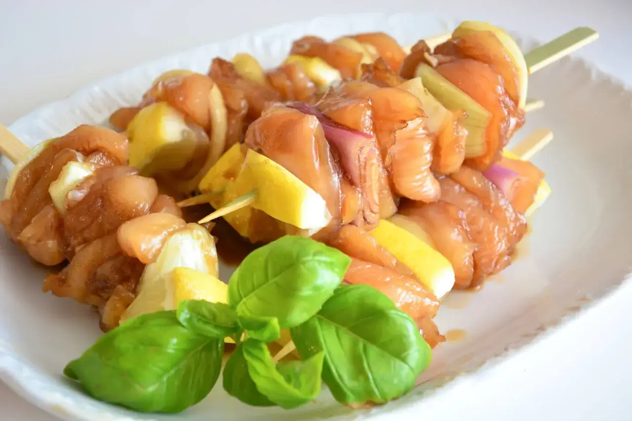 Sześć szaszłyków yakitori z kurczakiem, cebulą i cytryną na białym talerzu, ozdobione świeżą bazylią.