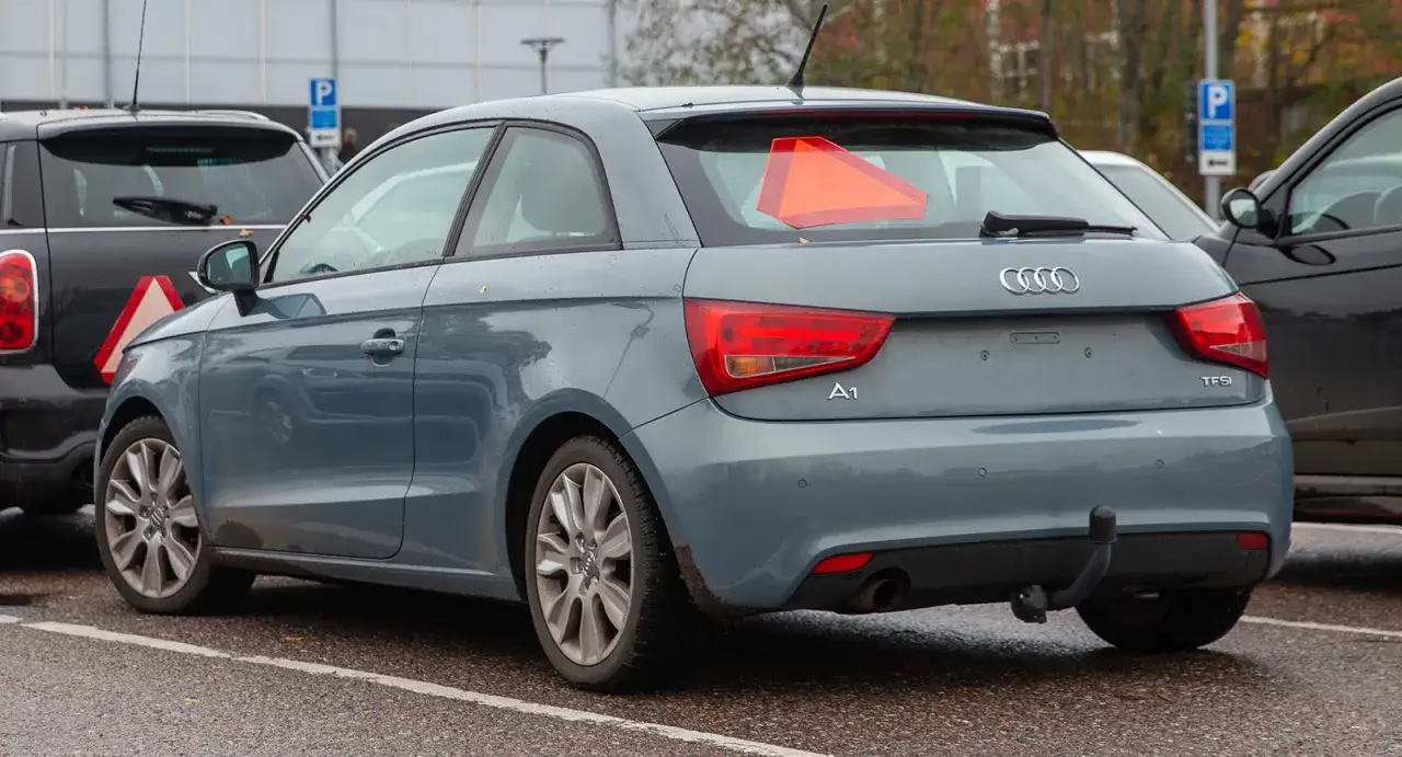 Gr&aring; Audi A1 med en varningstriangel p&aring; bakrutan. En traktor registreringsskylt &auml;r inte synlig.