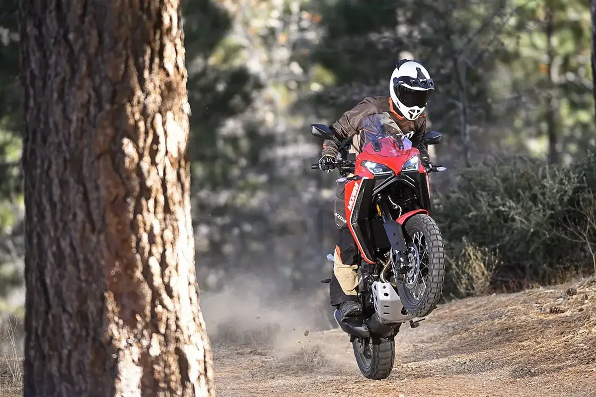 Motociclista en una Moto Morini X-Cape 650 roja haciendo un caballito en camino de tierra, levantando polvo. A pesar de su potencia, algunos usuarios reportan problemas.