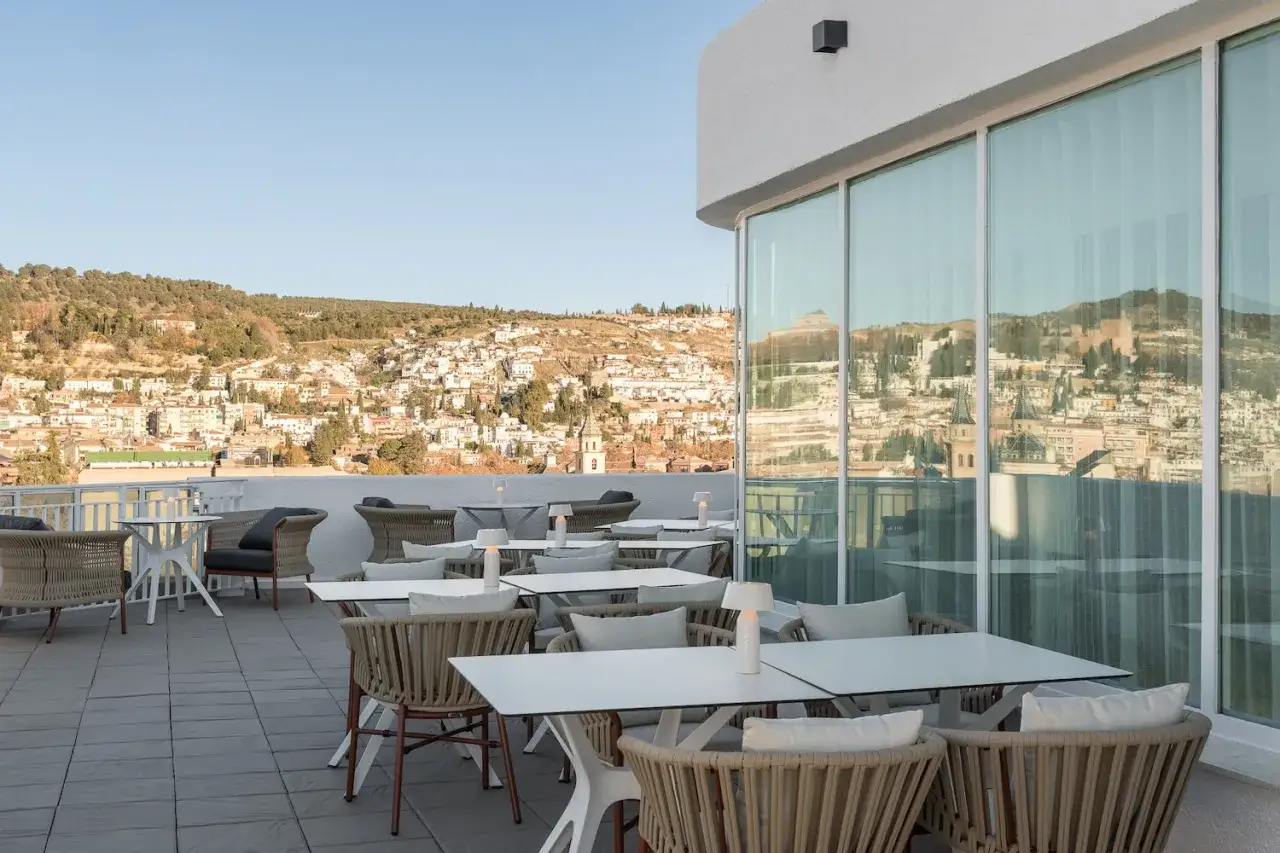 Terraza del hotel San Antón Granada con vistas a la Alhambra. Mesas y sillones de mimbre invitan a disfrutar del paisaje.