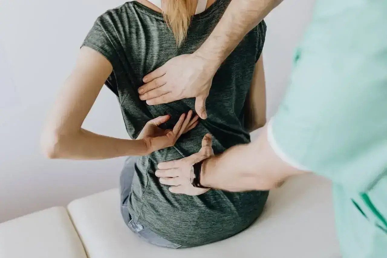 Fizjoterapeuta masuje plecy pacjentki, która potrzebuje l4 na rehabilitację. Dłonie terapeuty obejmują odcinek lędźwiowy kręgosłupa.