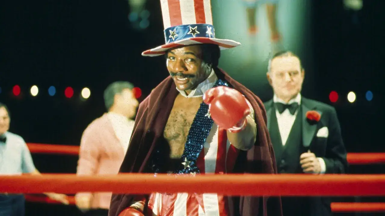 Carl Weathers w filmach jako Apollo Creed, w amerykańskim stroju, na ringu bokserskim.