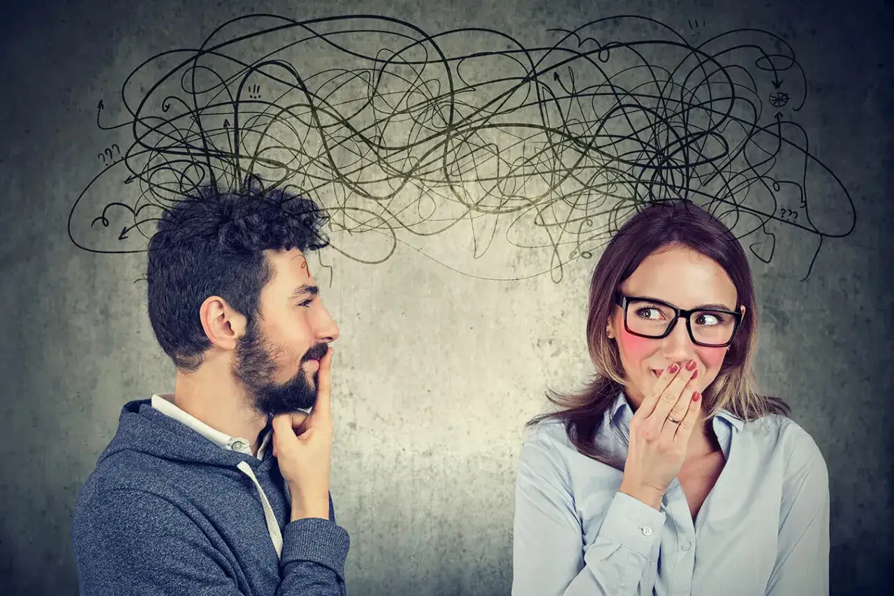 Uomo e donna con pensieri confusi sopra le teste. Lei copre la bocca, imbarazzata. Un'immagine che suggerisce come superare la timidezza.