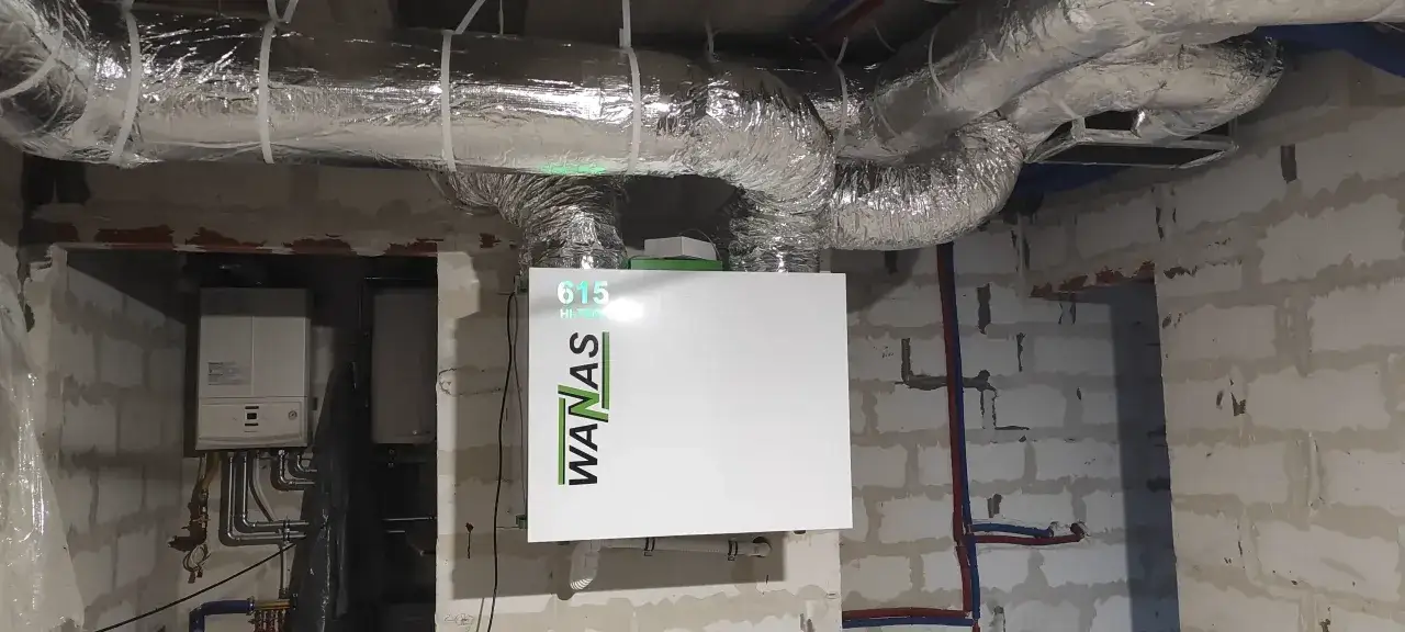 Nowoczesny rekuperator WANAS w kotłowni, podłączony do systemu wentylacji. Obok widoczny kocioł gazowy.