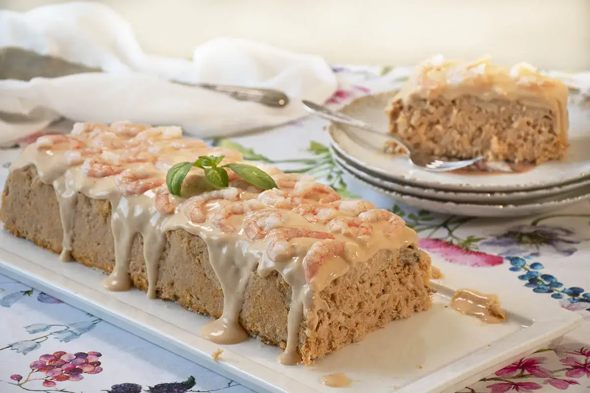 Un delicioso pudin de pescado cubierto con salsa rosada y camarones, decorado con una hoja de albahaca.