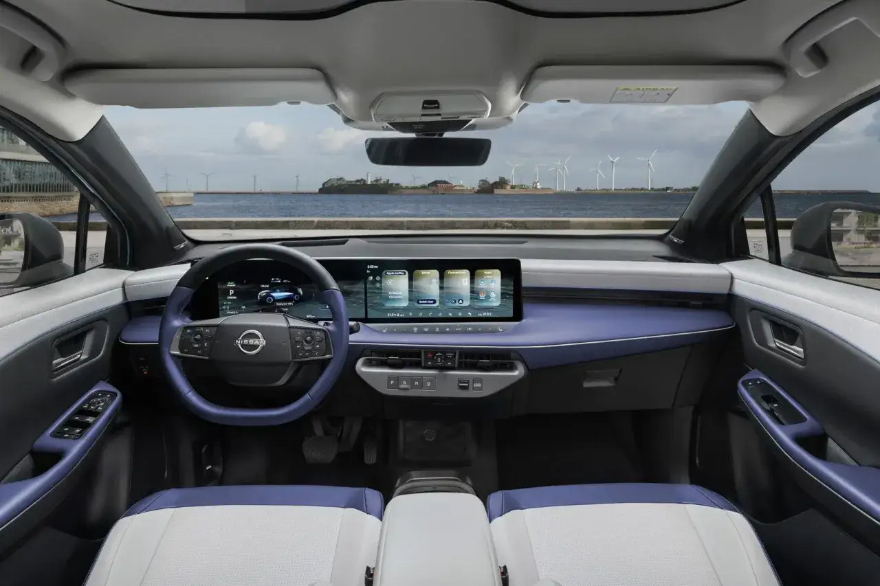 Wnętrze nowoczesnego nissan leaf elektryczny z niebieskimi akcentami i widokiem na morze z turbinami wiatrowymi.