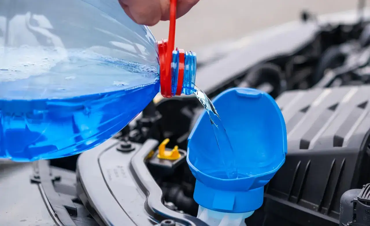 Blauer Scheibenreiniger wird in den Einfüllstutzen gegossen. So einfach kann man Scheibenwischwasser im Sommer selber machen.