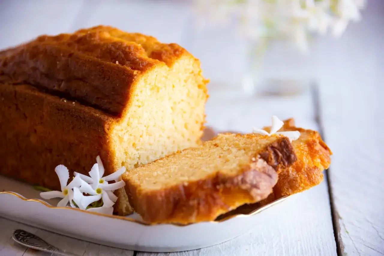 Un délicieux quatre-quarts doré, tranché et décoré de fleurs blanches sur une assiette élégante.