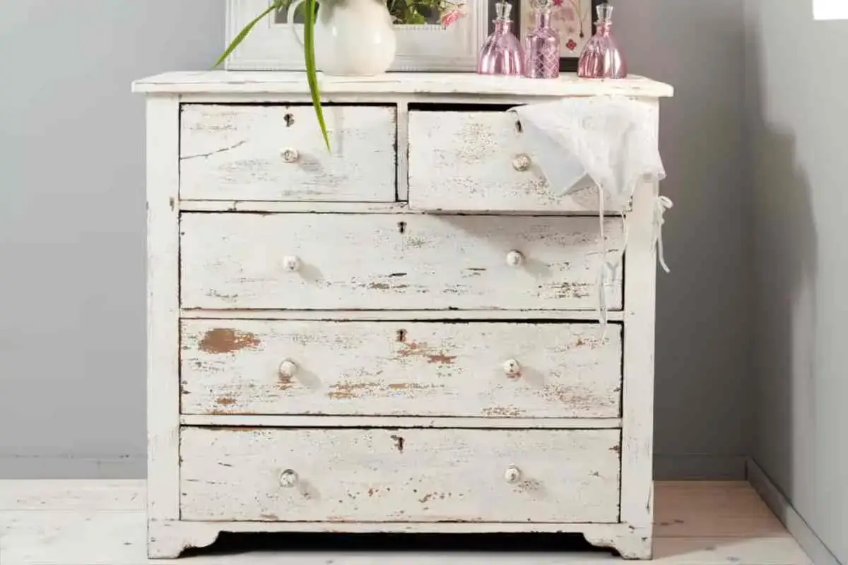 Comò con cassetti e un cassetto superiore, tutto in legno effetto invecchiato bianco, con maniglie rotonde e dettagli consumati.