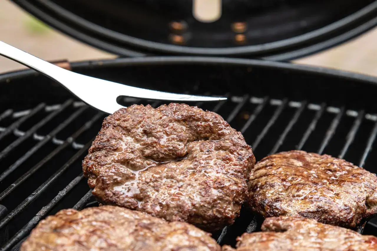 Saftige burger patties brutzeln auf dem Grill. Eine Grillgabel liegt daneben, bereit zum Wenden.