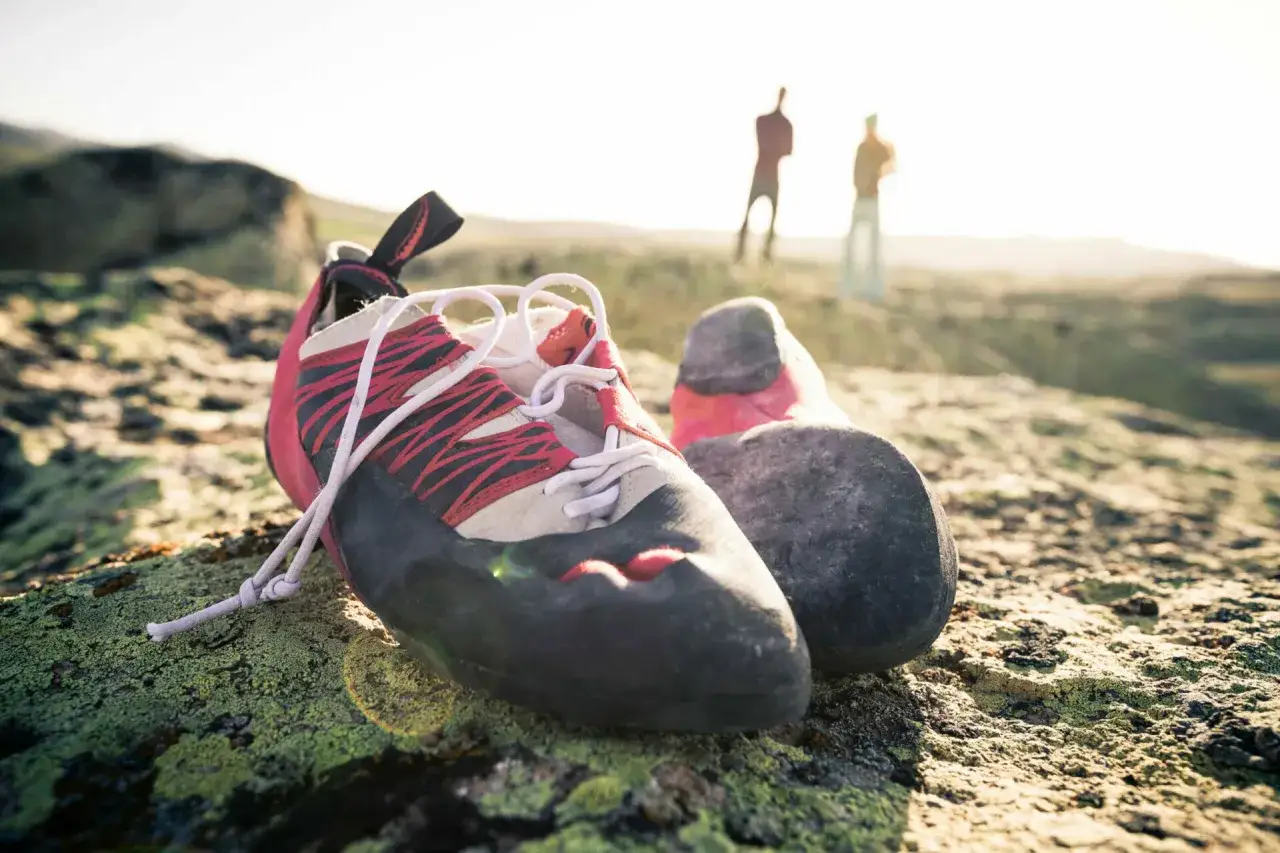 Kletterschuhe liegen auf einem moosbewachsenen Felsen. Im Hintergrund stehen zwei Kletterer. Zeit f&uuml;r kletterschuhe waschen nach einem langen Tag.