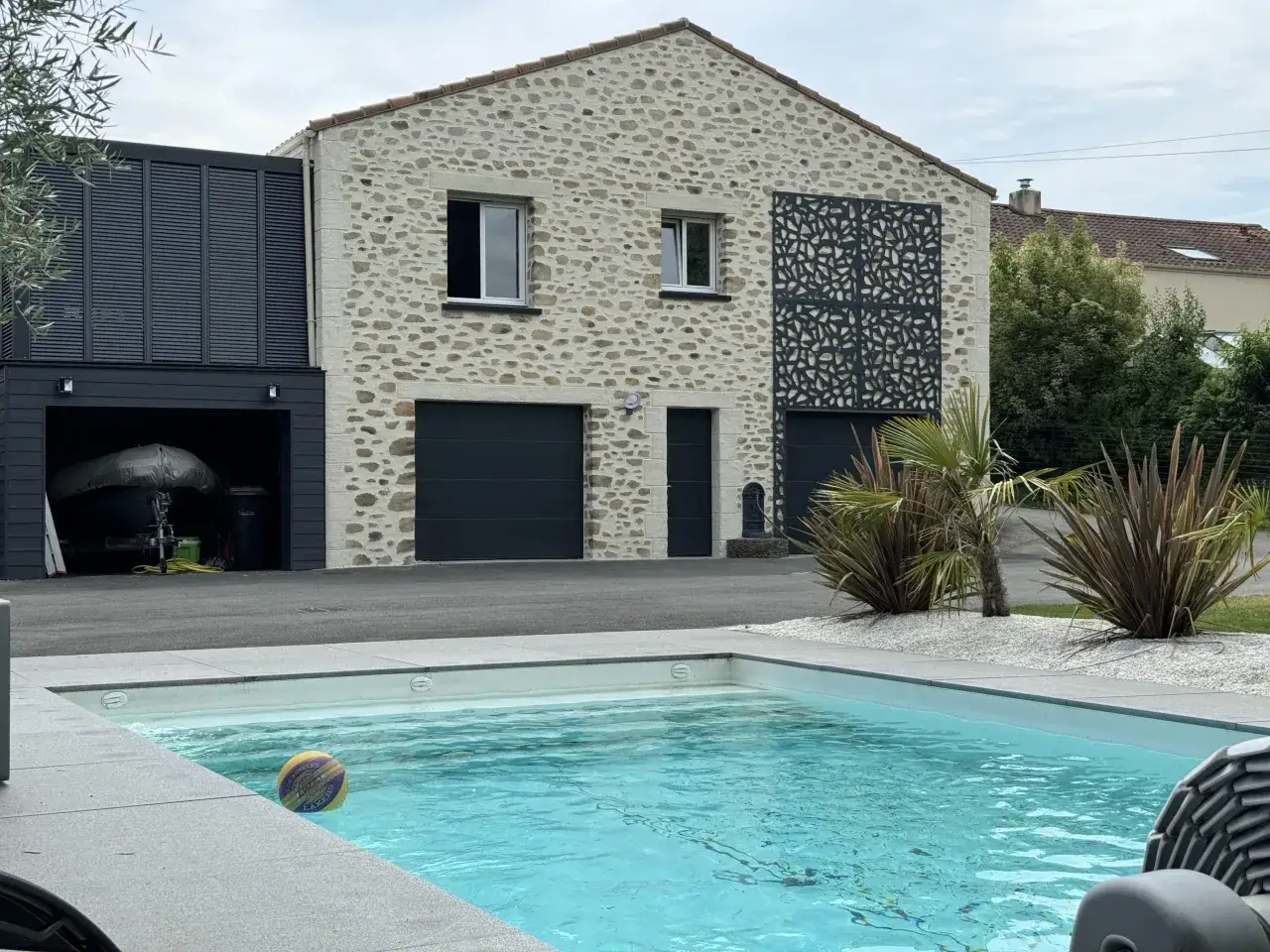 Fa&ccedil;ade maison en pierre avec garage, piscine et ballon de basket.