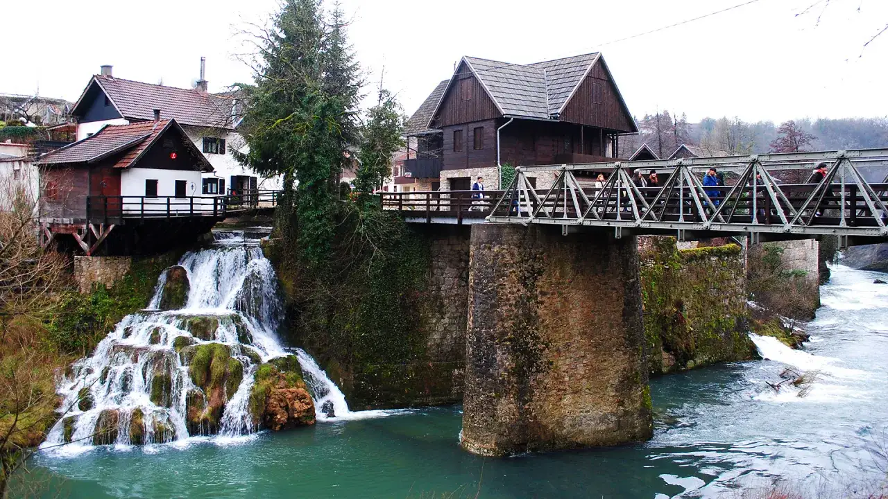 Rastoke, Croazia: cascate e mulini sull'acqua. Un ponte metallico attraversa il fiume, collegando case tradizionali con tetti spioventi.