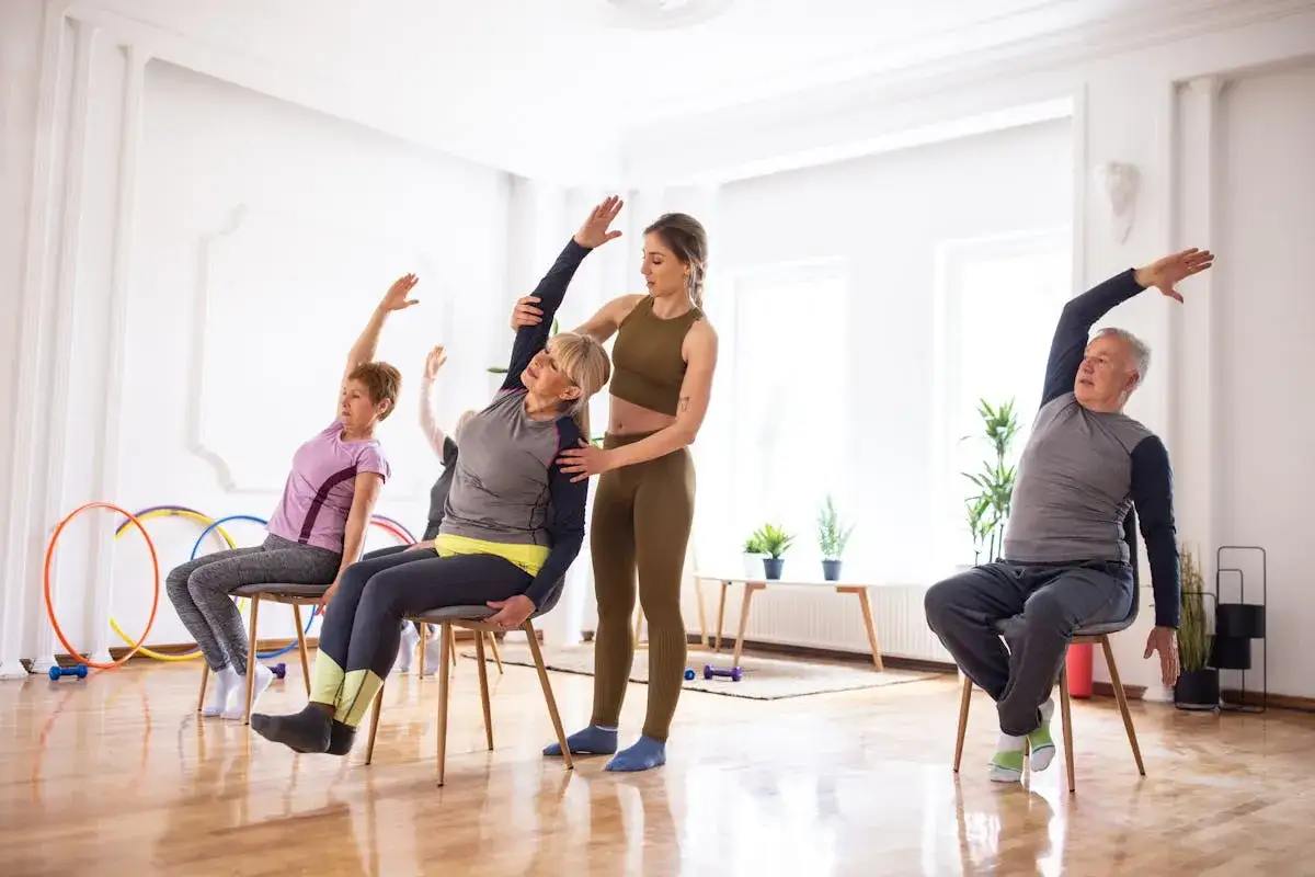 Cours de pilates pour femme de 60 ans et plus, avec une monitrice guidant des seniors dans des étirements assis.