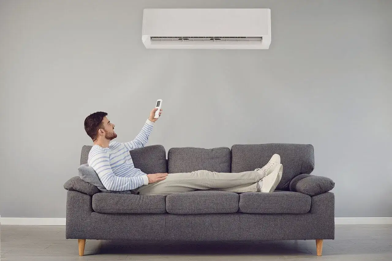 Mężczyzna na kanapie steruje klimatyzatorem. Klimatyzator 2.5 kW na ile metrów zapewni komfort?