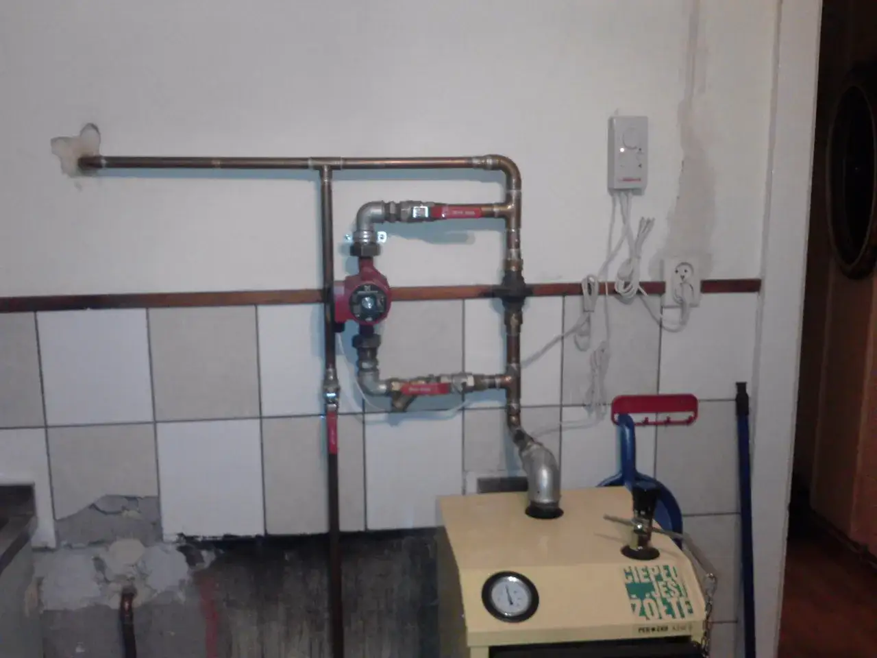 Montaż pompy CO w układzie otwartym. Widoczna instalacja miedziana, czerwona pompa obiegowa i fragment kotła.