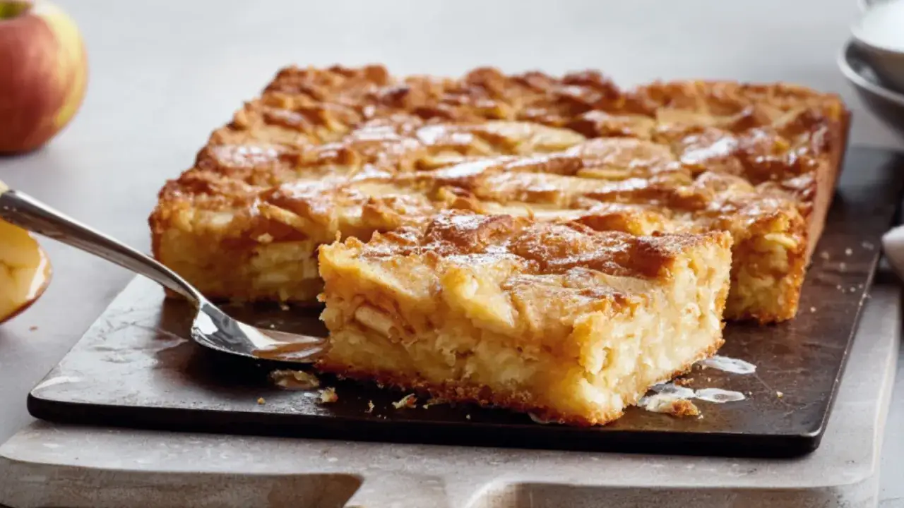 Saftige schwedische Apfeltorte, mit Zimt und Zucker bestreut, auf einem rustikalen Brett, daneben ein Löffel mit einem Stück Torte.