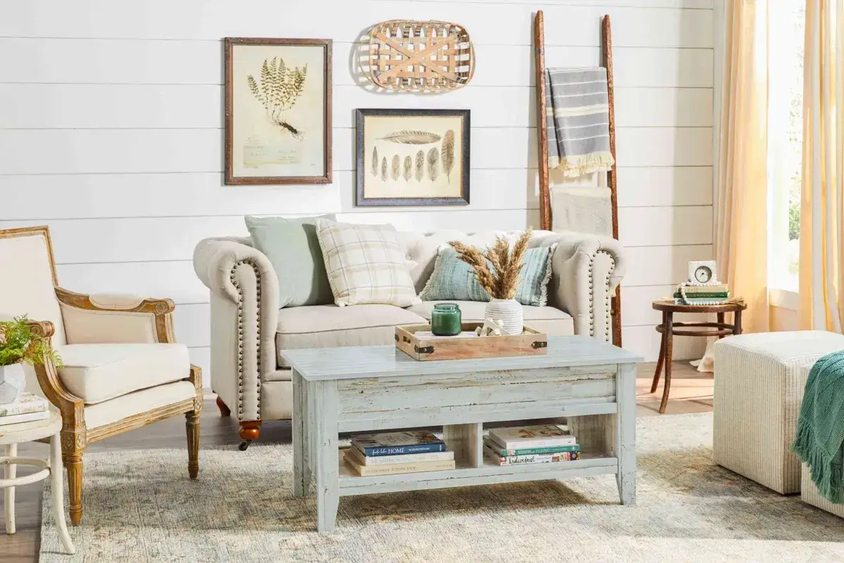 En soffa och fåtölj i shabby chic inredning. Ett soffbord med förvaring, kuddar och en vas med torkade blommor.